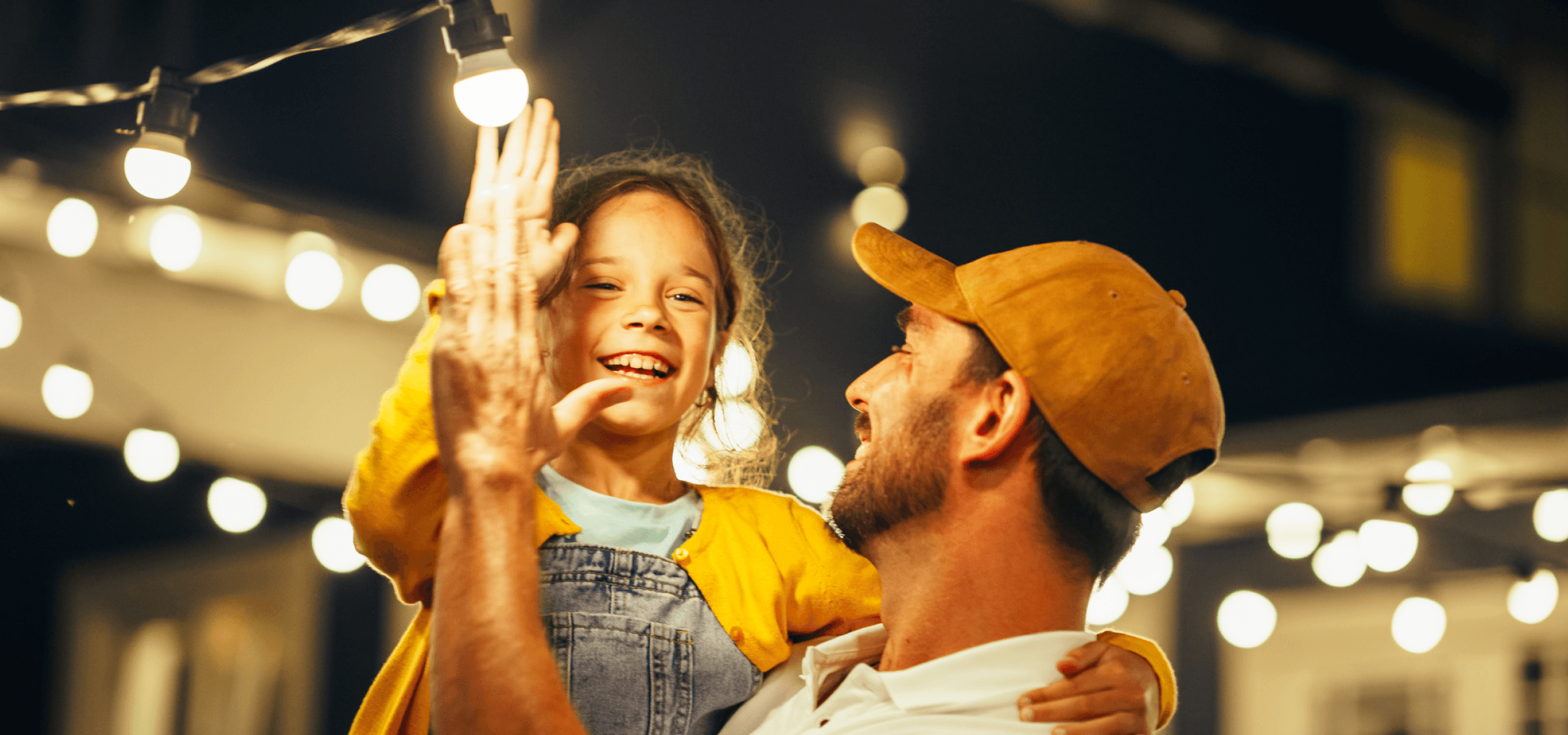 Image of father and daugther under electrical bulbs at night.